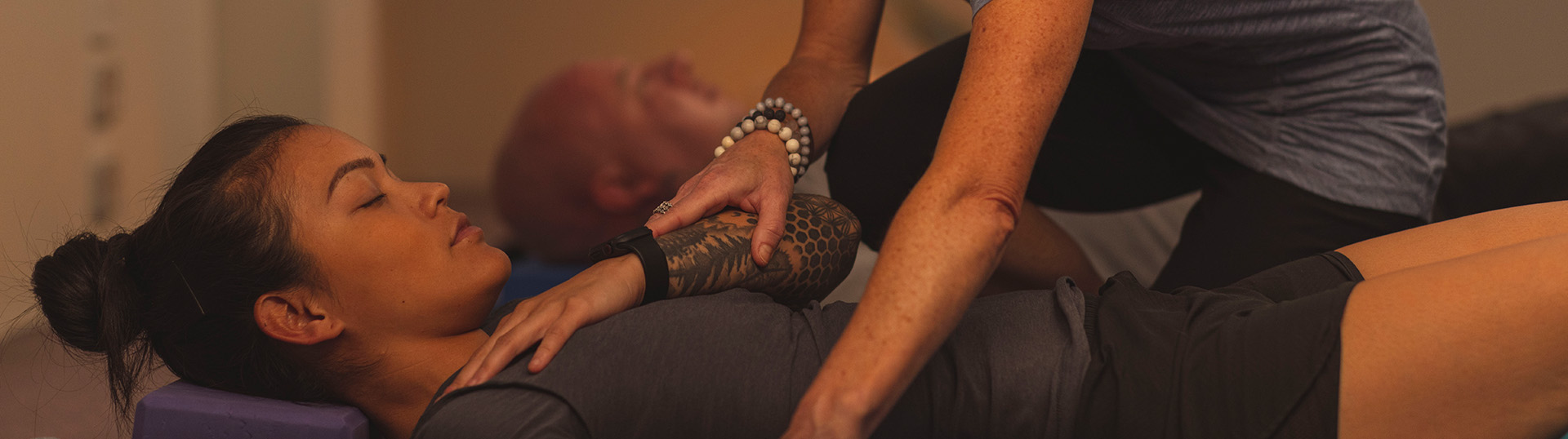 A Mates4Mates staff member supporting a client's laying form in a trauma informed yoga session.