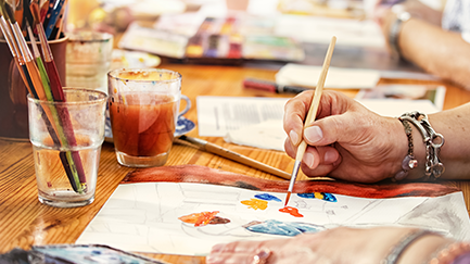 Hand resting on an art table holding a paintbrush. Painting on a piece of paper 