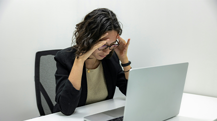 Woman leaning over laptop holding her head. 
