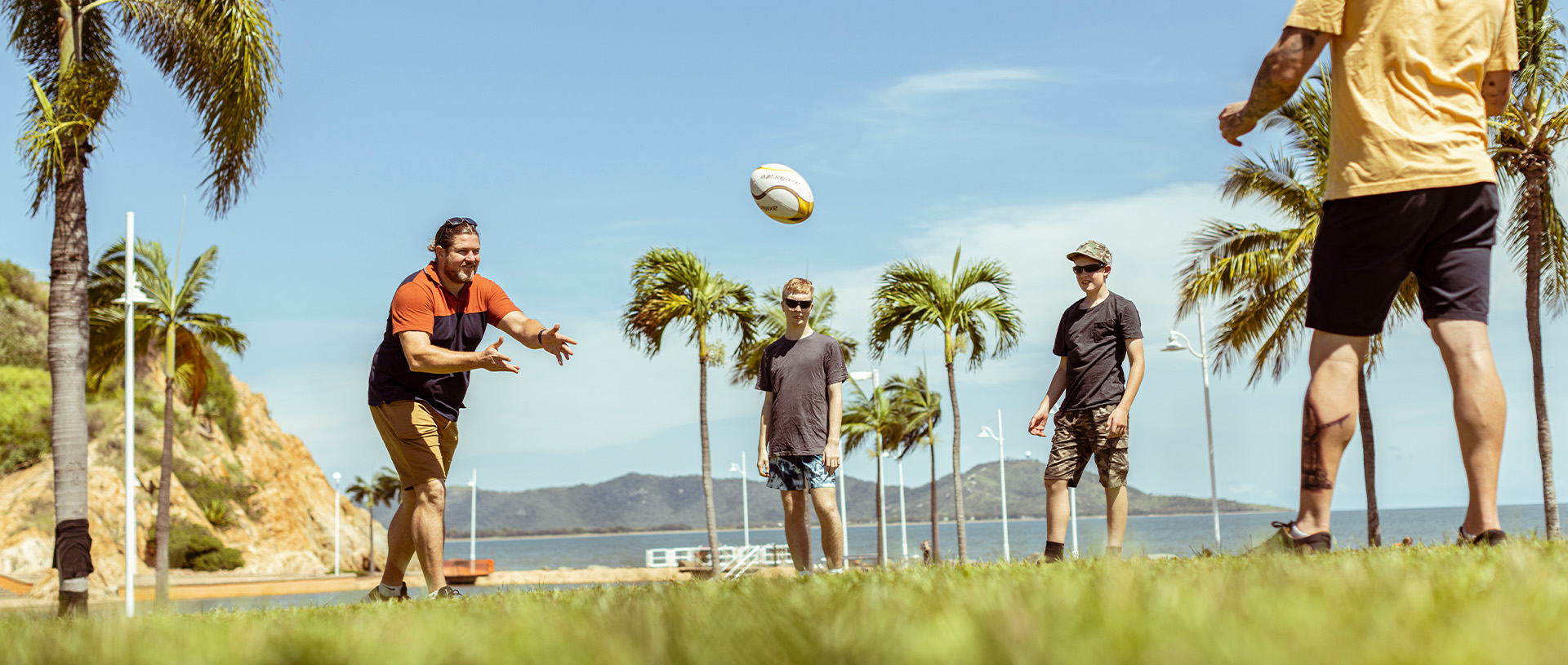 Group playing throwing a rugby ball together in a park on a clear blue day.