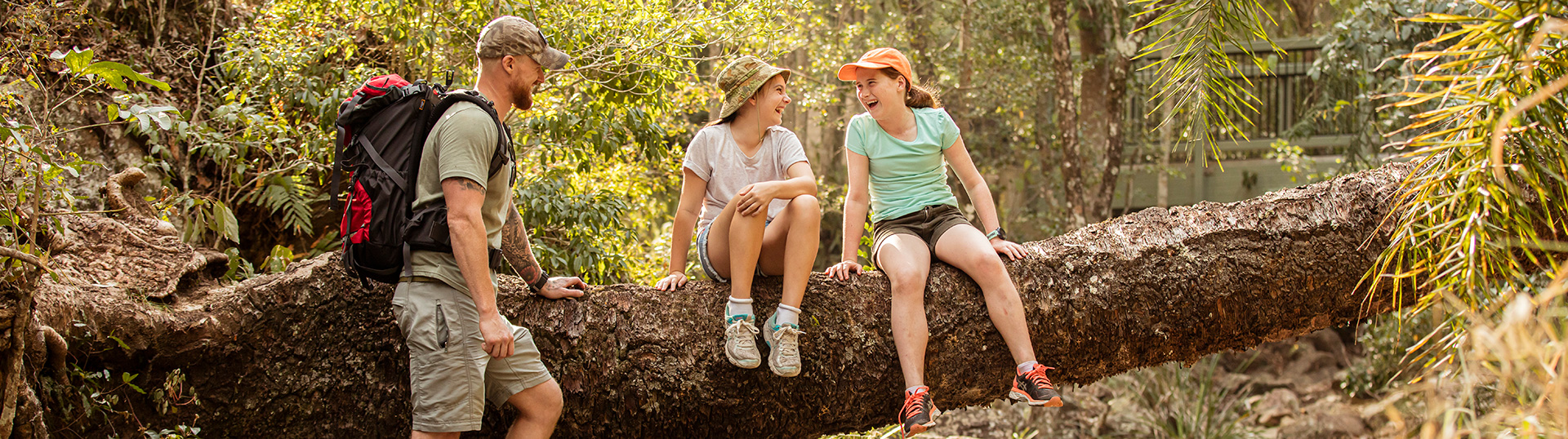 Girls sitting on a log laughing together with their father standing close