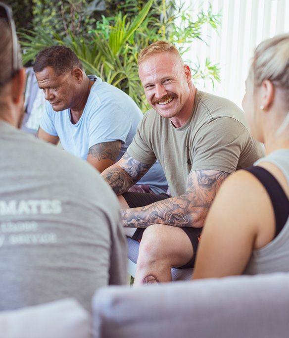 Group sitting together having a coffee and a chat, one person is smiling at the camera.