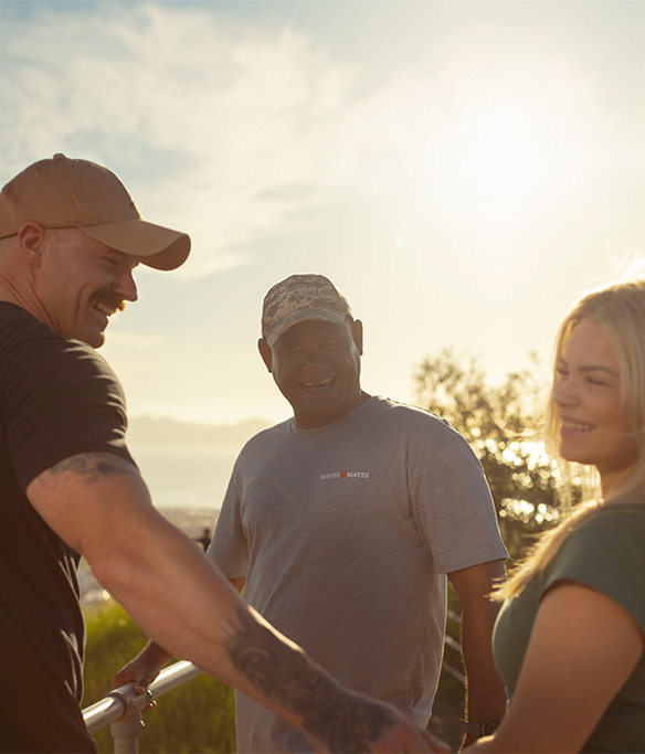 Three people standing in the late afternoon laughing together.