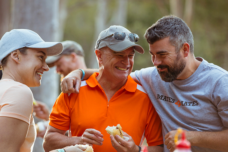 Group of three huddled together laughing while they enjoy a BBQ