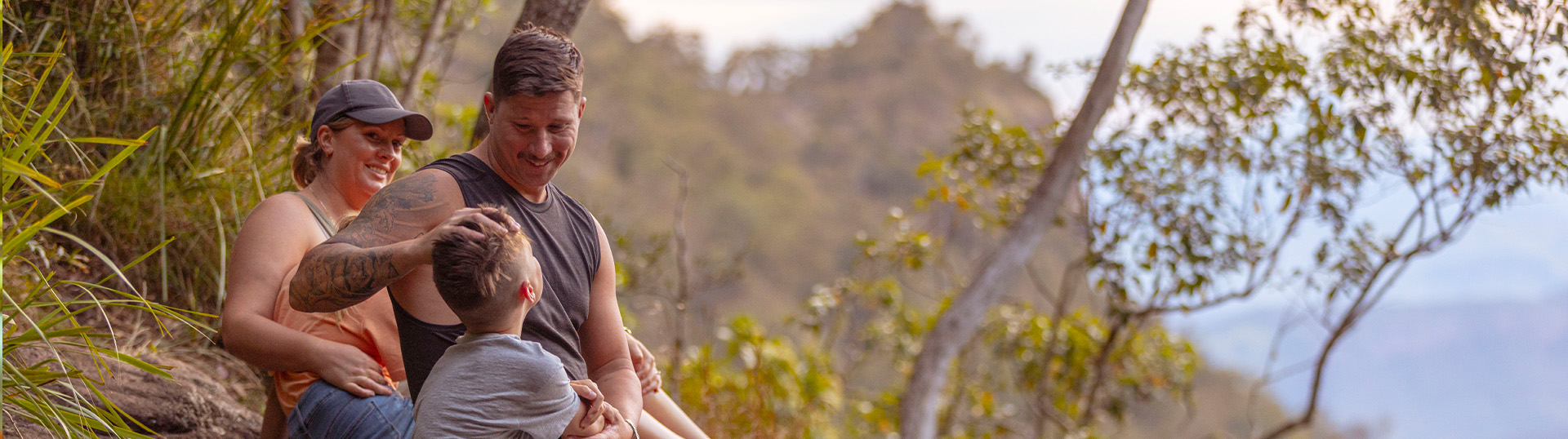 Family sitting together outdoors with a father messing the hair of his young son.