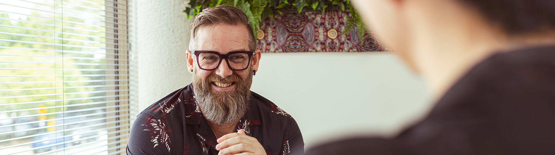 Male patient with black glasses and a long grey beard smiling in a counselling session.