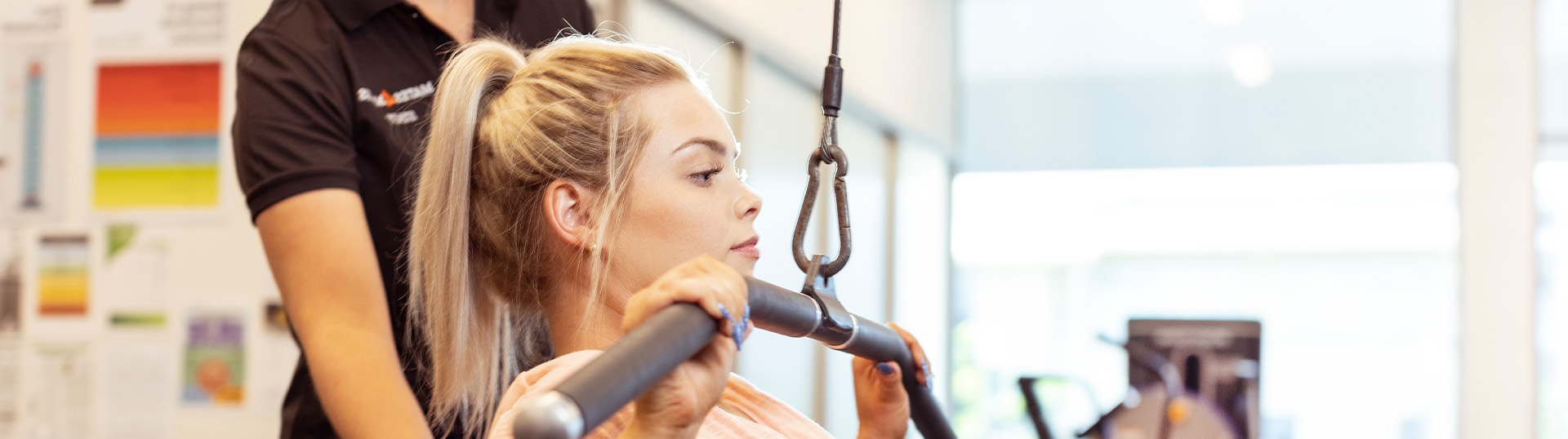 A woman using gym equipment with the assistance of an exercise physiologist.