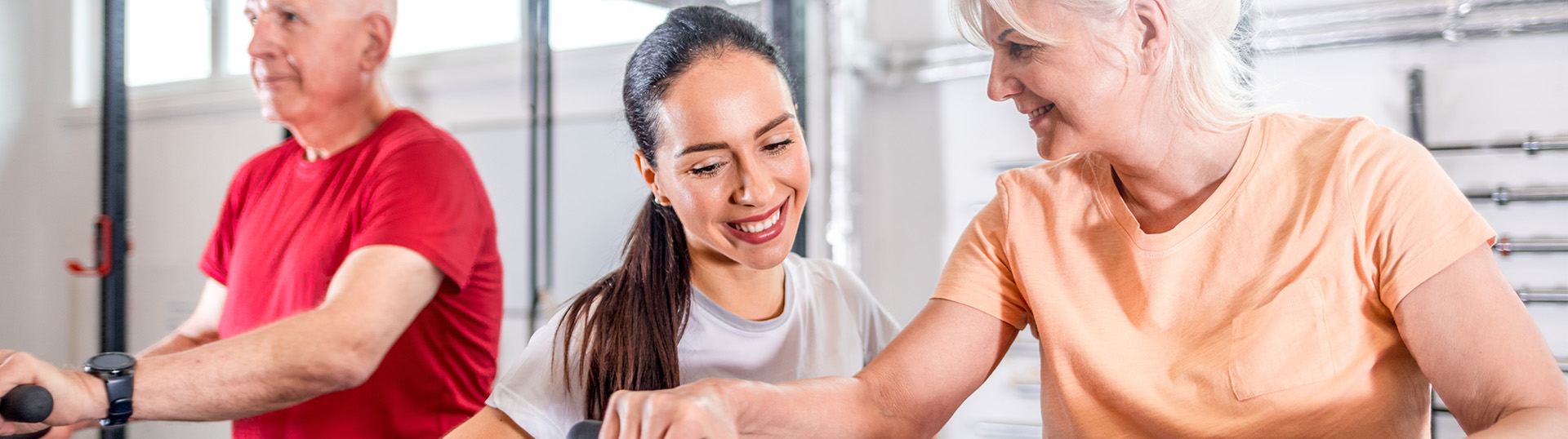 Two older people on exercise equipment with an instructor close