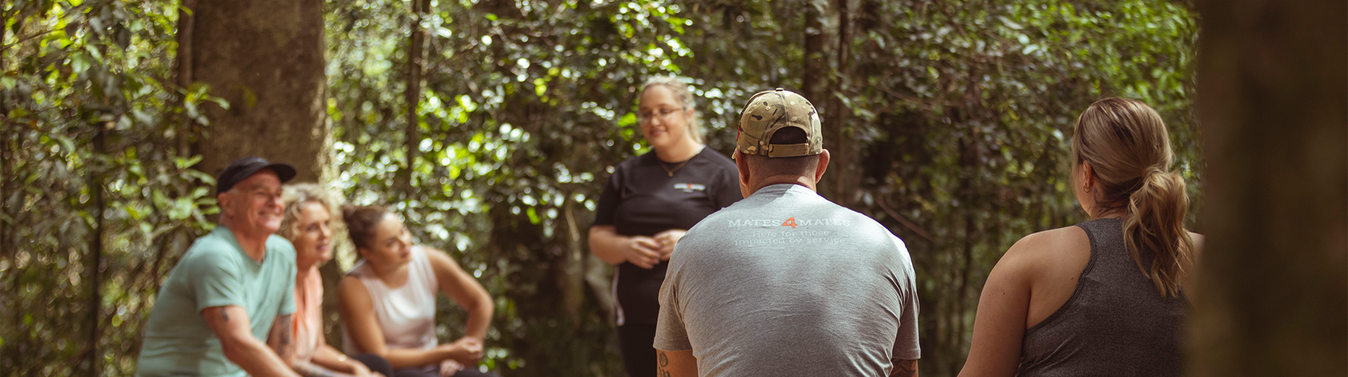 A group of veterans and family members sitting outdoors listening to an instructor.