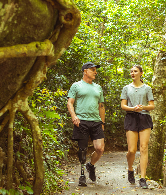 Two people walking through a forest path talking.