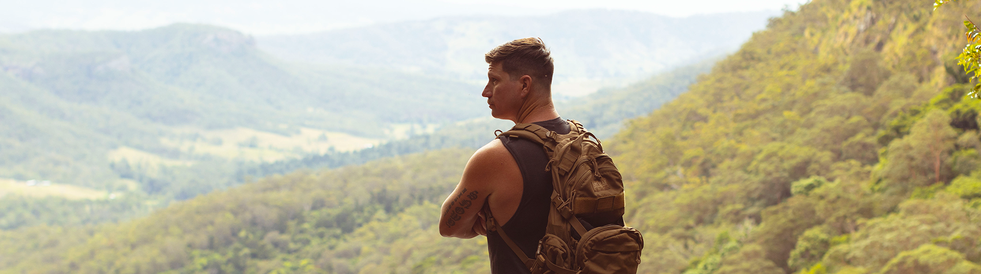 Male veteran standing arms crossed, taking a break from a hike to look out over the view of the national park, wearing a backpack.