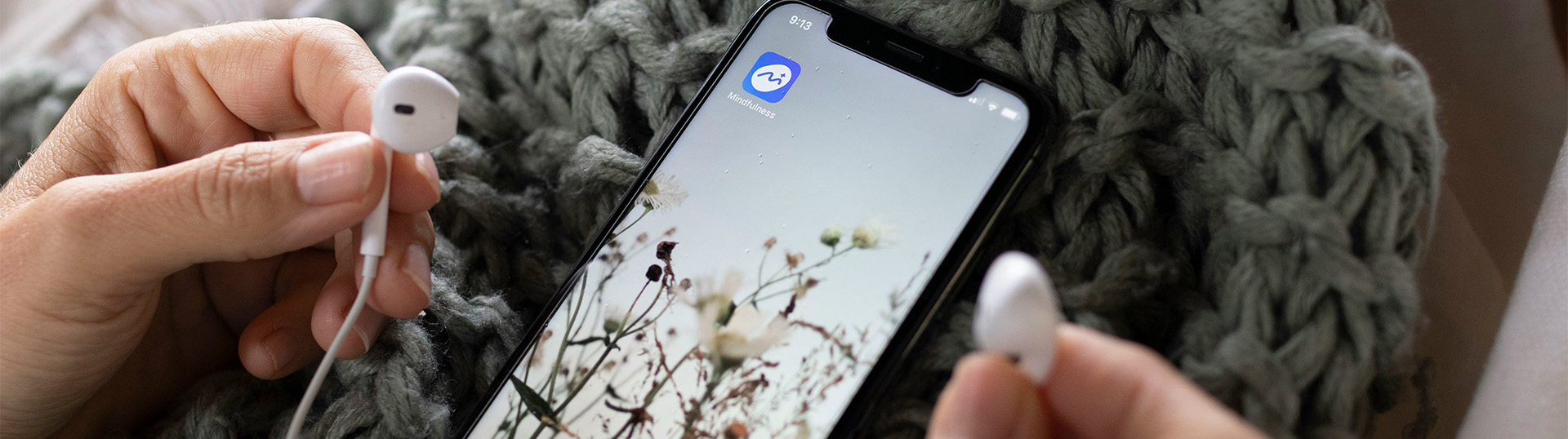 Phone laying on a person's lap, ear phones being held in hands.