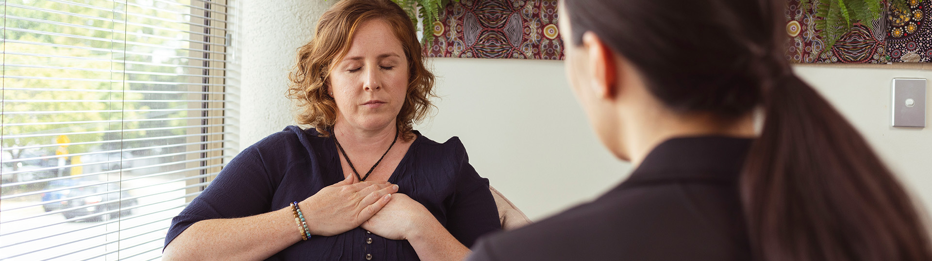 Woman sitting in a mental health appointment with their hands over their heart.